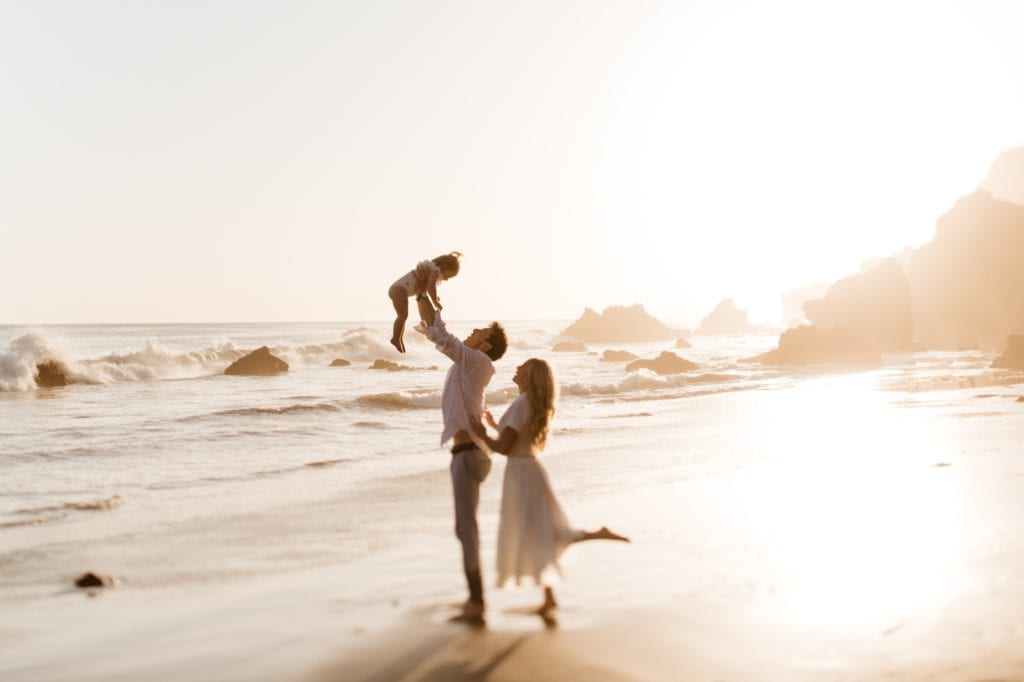 Parents lifting up their one year old baby girl on the beach in Malibu during sunset
