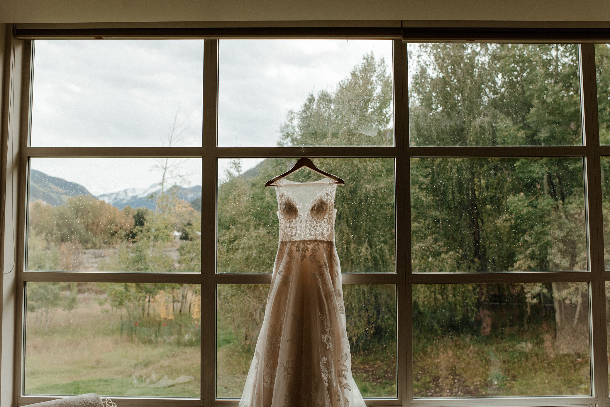 a wedding dress hangs from the floor to ceiling window at Aspen Meadows Resort