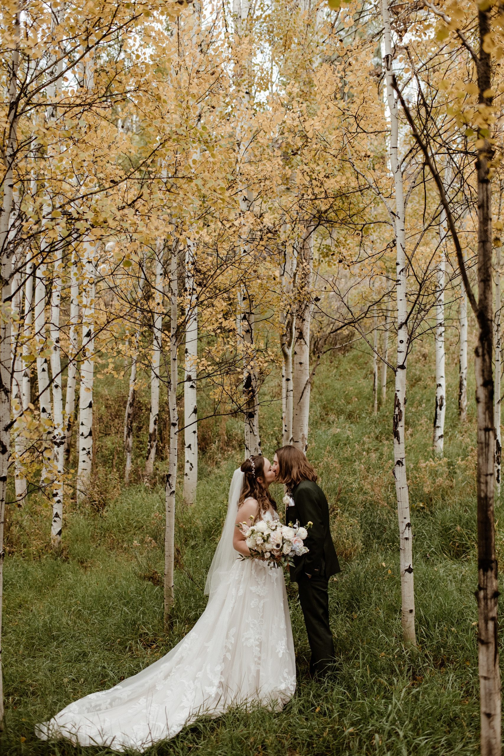 A bride and groom walk among the aspens at Aspen Meadows Resort