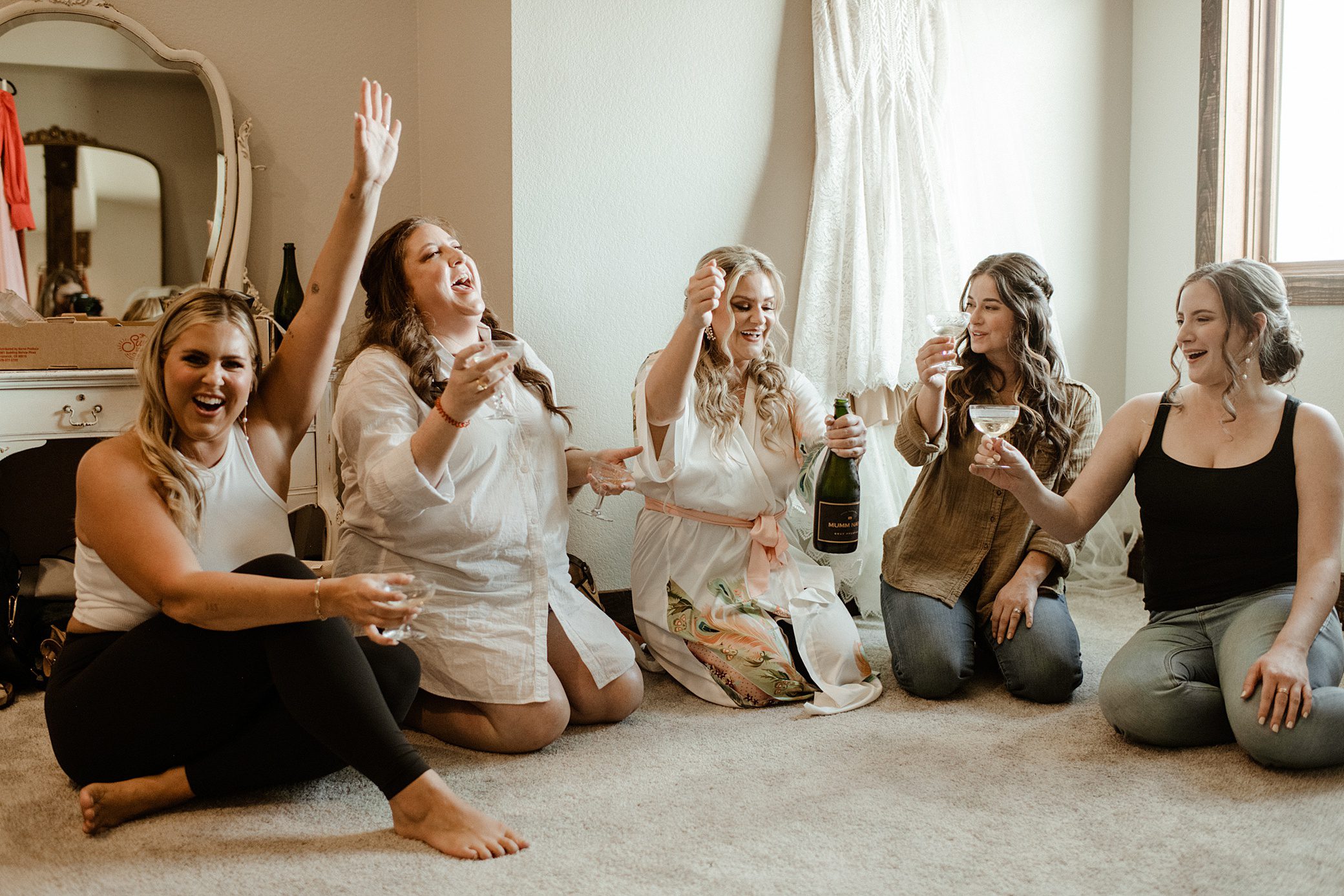 A bride and bridesmaids hang out together on the floor while getting ready for a wedding at the Barn at Sunset Ranch in Buena Vista, CO