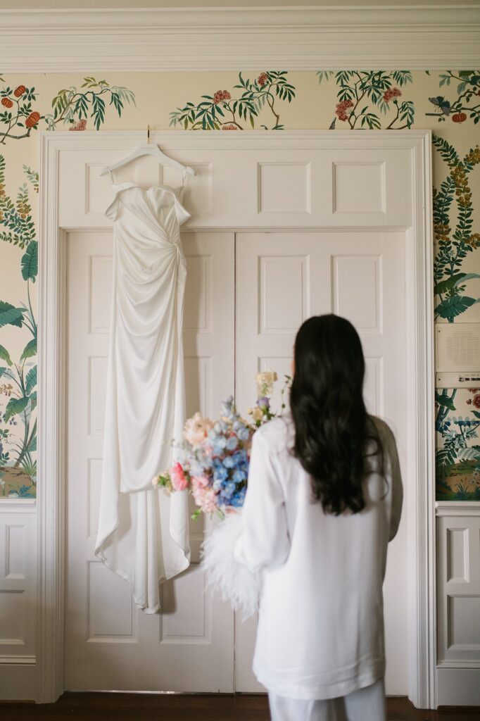 a bride looks at her wedding dress hanging from the door before her Greystone Castle wedding