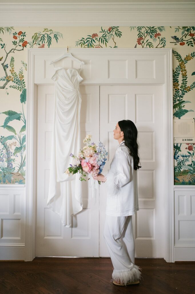 a bride looking up at her wedding dress hanging from the door before her Greystone Castle wedding.
