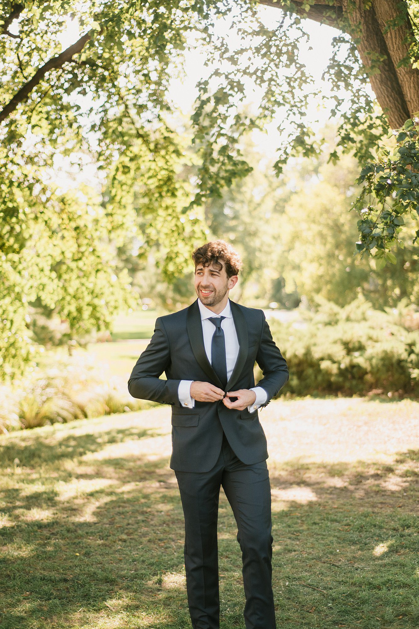 a groom poses in the shade of the trees prior to his Washington Park Boathouse wedding in downtown Denver