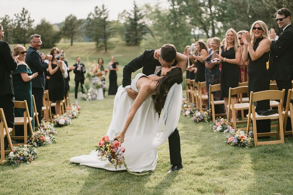 a groom dips his bride in the aisle after their Lower Spruce Mountain Ranch wedding ceremony