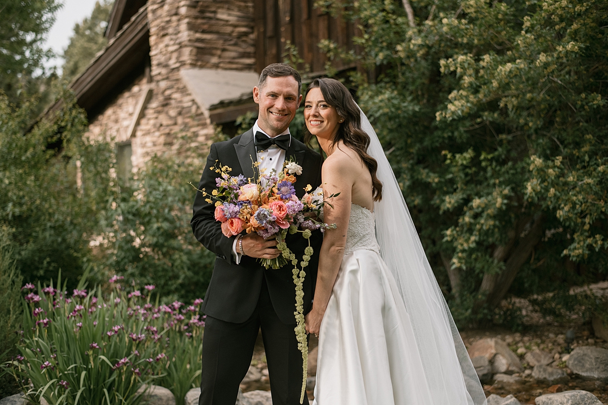 A bride and groom pose together immediately after their Lower Spruce Mountain Ranch wedding ceremony near the stone cabin
