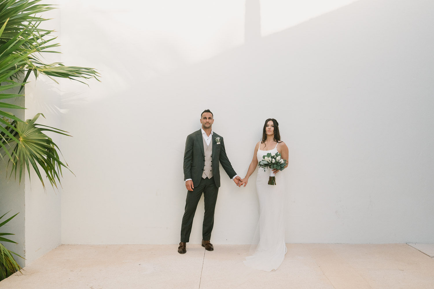 A bride and groom against a white wall after their Finest Playa Mujeres wedding in Cancun, Mexico